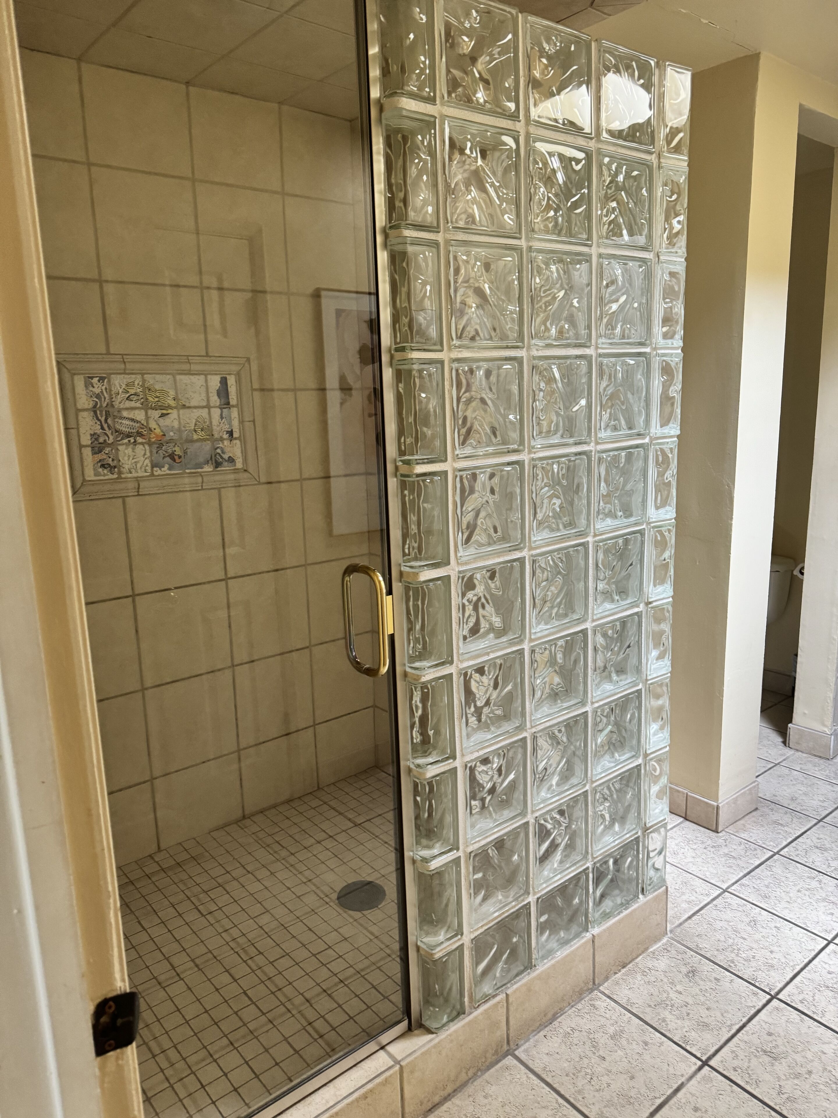 A glass-enclosed shower with a tiled floor and a decorative panel on the door.