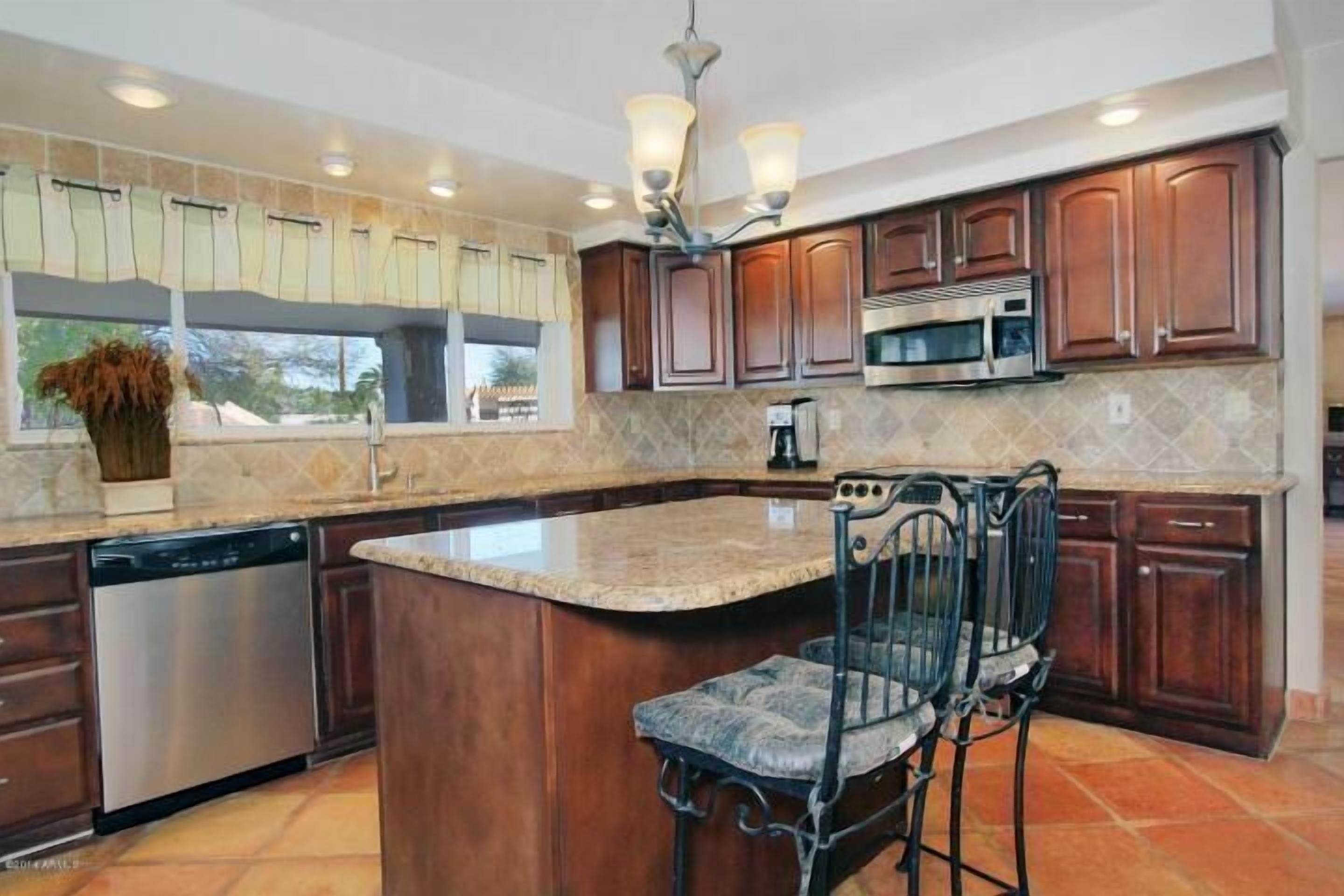 A kitchen with wooden cabinets, a stainless steel dishwasher, a built-in microwave, and a large island with a bar stool.