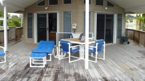 Um deck coberto ao ar livre com uma mesa e cadeiras azuis, uma porta de correr de vidro e um deck de madeira.