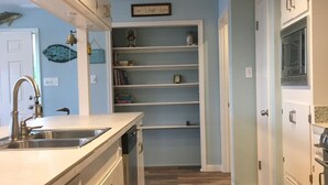 Cozinha com armários brancos, pia de aço inoxidável e lava-louças. Há prateleiras abertas com livros e objetos decorativos.