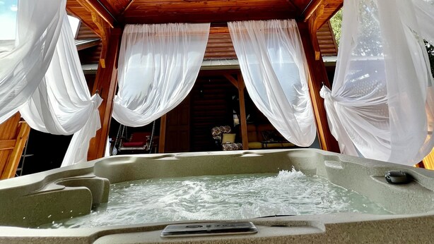 L'intérieur d'un chalet en bois, avec un jacuzzi et des rideaux blancs.
