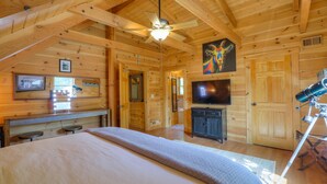 Une chambre située dans un chalet en rondins, équipée d’un lit, d’un ventilateur de plafond, d’une télévision et d’un télescope.