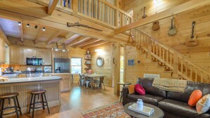 L’intérieur de cette vaste cabane en rondins comprend une cuisine, un coin repas et un salon confortable, avec un canapé en cuir et un escalier.