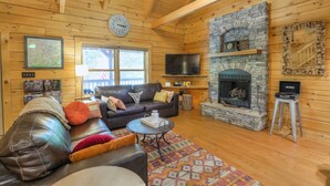 Un intérieur de chalet chaleureux avec une cheminée en pierre, un canapé en cuir et un téléviseur à écran plat.