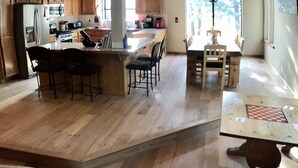 A spacious kitchen with wooden cabinets, a central island with bar stools, and a dining area with a large window. - Winter wonderland perfect for multiple families- 3 master bedrooms! (Truckee)