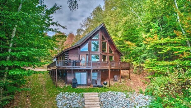 Eine Blockhütte mit Balkon, Veranda und einem Steinweg, der zum Eingang führt.