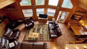 Ein Blockhaus-Interieur mit Kamin, Ledersofas, Fernseher und großen Fenstern.