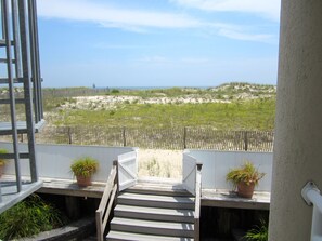Eine Holztreppe führt zu einem Balkon mit Blick auf einen Sandstrand und Dünen.