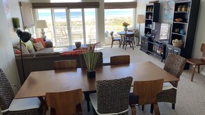 A spacious living room with a large dining table, comfortable seating, a bookshelf, and a view of the beach. - Oceanfront 12 Bedroom 8 Bath in Ocean City, New Jersey (Ocean City)