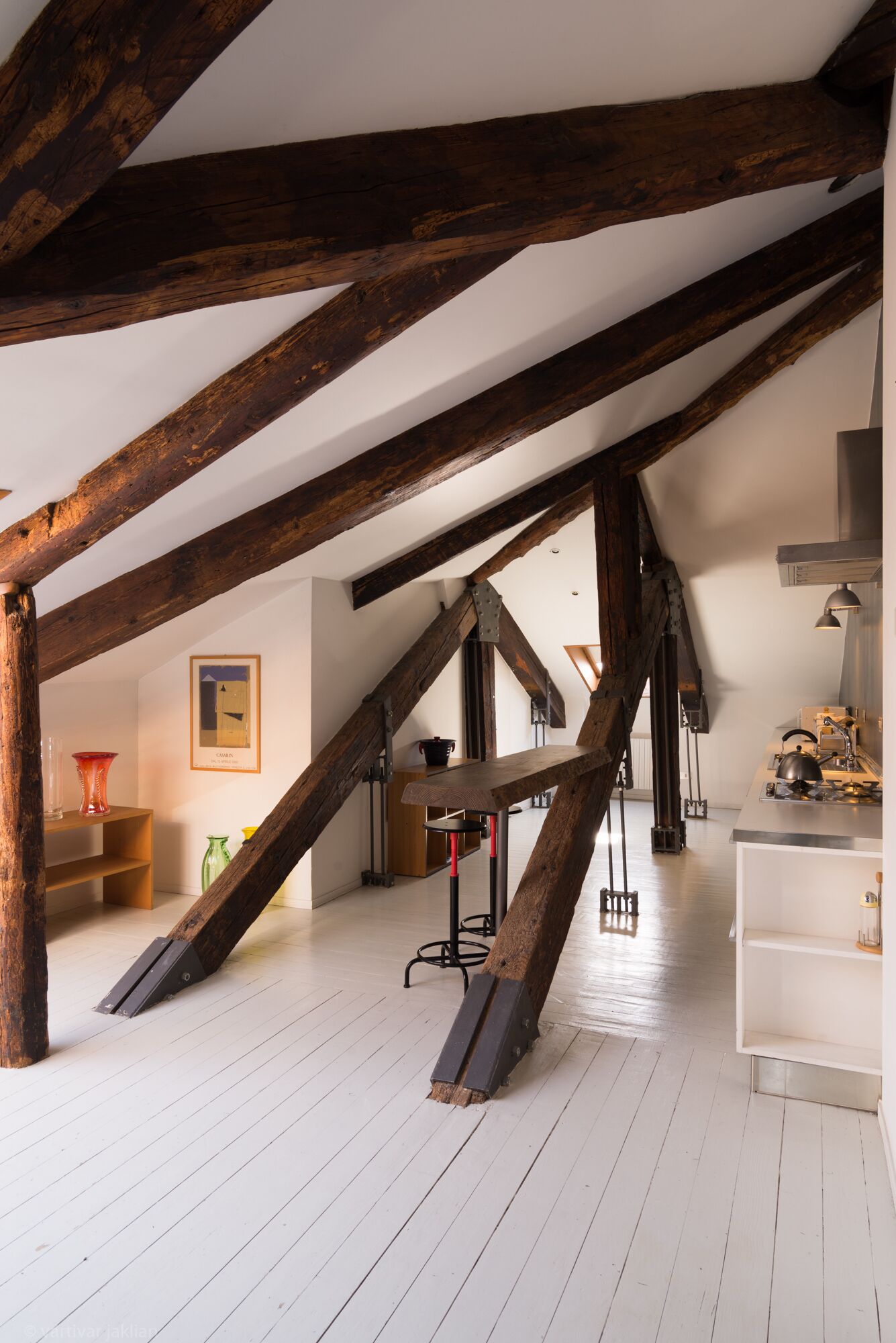 Una habitación con vigas de madera a la vista, una zona de cocina y una mesa de comedor.