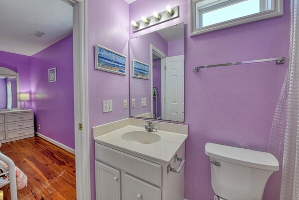 A bathroom with purple walls, a white sink, a mirror, and a toilet.