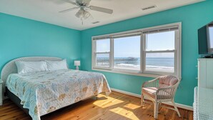 A bedroom with a bed, a chair, a TV, and a window with a view of the beach. - Against The Wind A, Oceanfront Home, Amazing Pier View, Duplex (Garden City Beach)