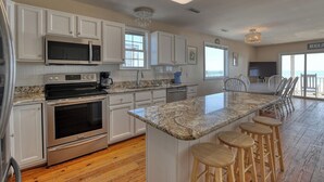 A kitchen with white cabinets, stainless steel appliances, a granite countertop, and a bar area with stools. - Against The Wind A, Oceanfront Home, Amazing Pier View, Duplex (Garden City Beach)