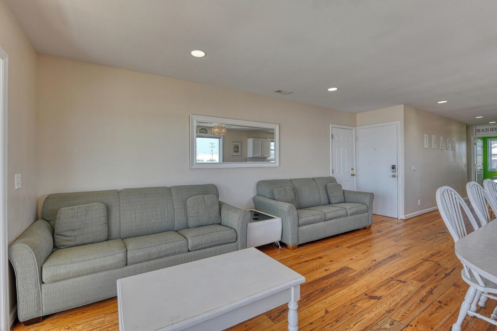 A living room with two grey sofas, a white coffee table, and a dining area with white chairs.
