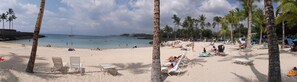 A beach with palm trees, clear water, and people swimming.