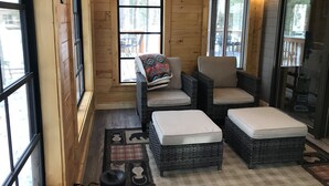 A cozy log cabin interior with wicker furniture, large windows, and a checkered rug. - Executive Year Round Home ~ Minutes From  Minocqua (Arbor Vitae)
