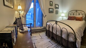 Une chambre à coucher avec un lit, un bureau avec des livres, une chaise, une fenêtre avec des rideaux et des lampes fixées au mur.