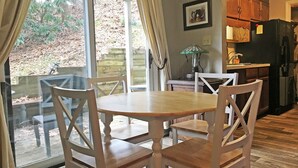 Un coin repas avec une table et des chaises, une cuisine avec des meubles en bois, un réfrigérateur et une fenêtre avec des rideaux.