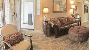 Un salon comprenant un canapé, un pouf et des fauteuils, un parquet et, au fond, un coin repas.
