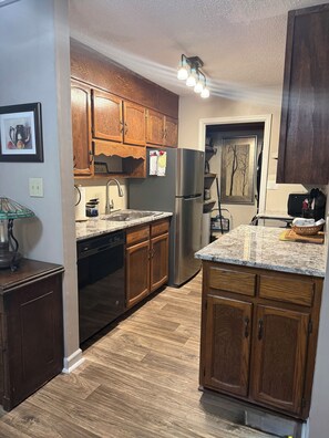A kitchen with wooden cabinets, a stainless steel refrigerator, a dishwasher, and a granite countertop.