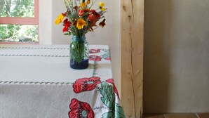 A room with a wooden ceiling, a table with a floral tablecloth, a vase with flowers, and a framed picture on the wall. - Unsurpassed Night Skies And Fresh Mountain Air In A Traditional Village (Santa Fe)