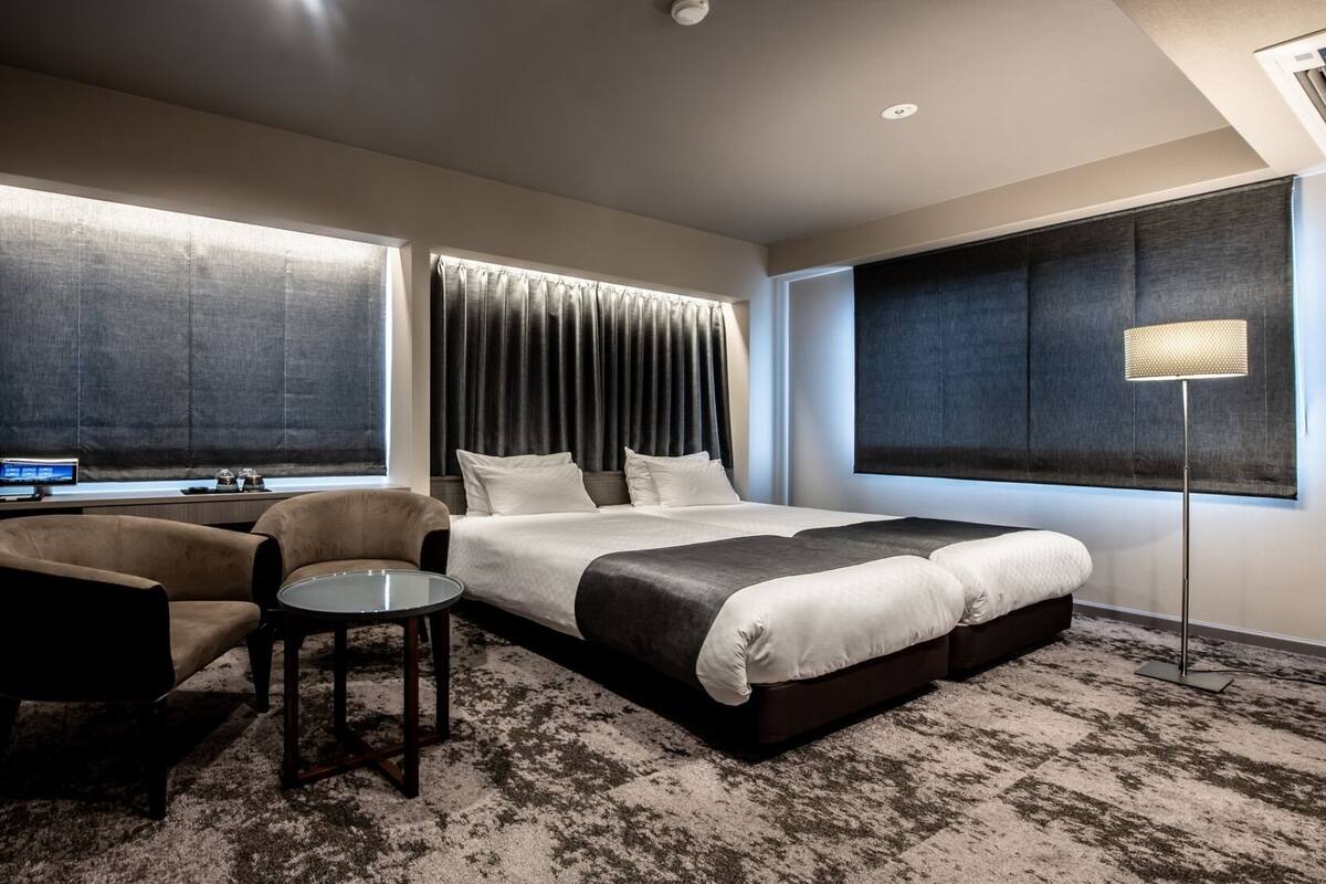 Habitación de hotel con cama, escritorio con computadora, silla, mesita y lámpara de pie.