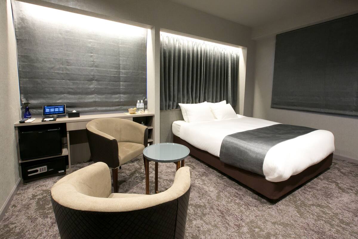 Una habitación de hotel con una cama, un escritorio con una computadora, una silla y una mesita.