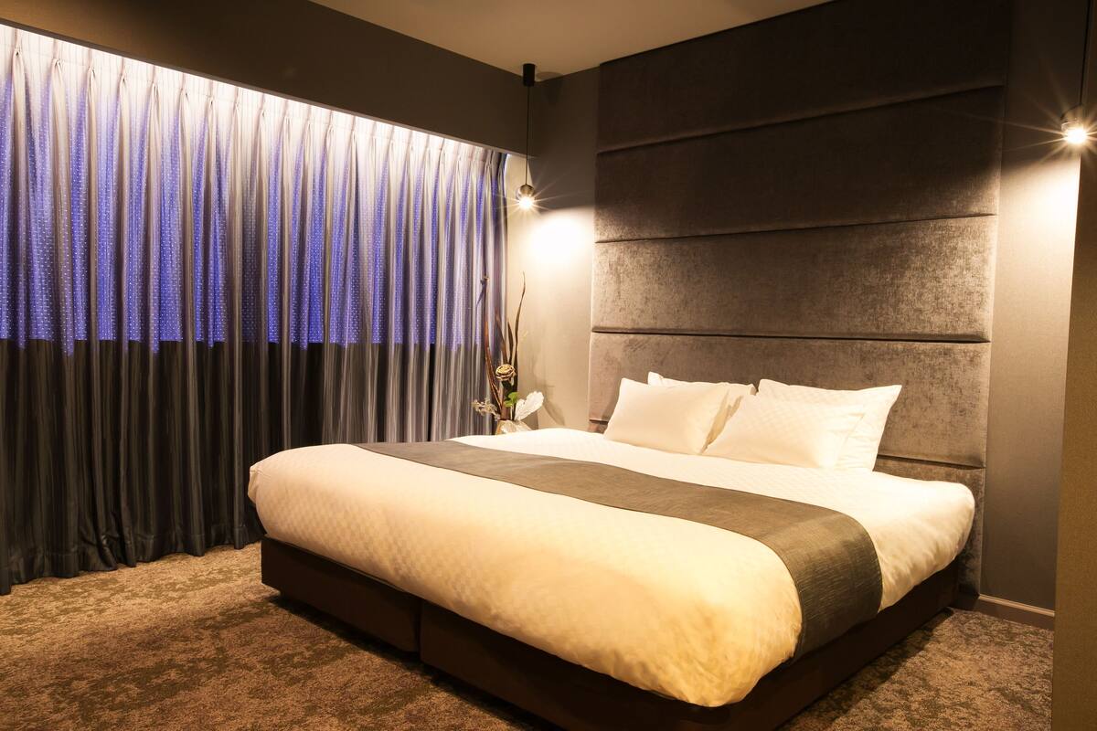 Un dormitorio moderno con una cama grande, cabecera oscura y una ventana con cortinas.