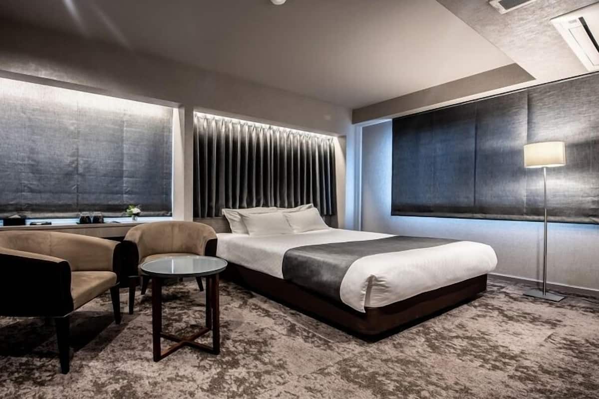 Quarto de hotel moderno com uma cama grande, uma escrivaninha com computador, uma cadeira e uma mesa pequena.