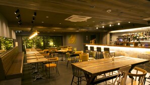 Un restaurante con largas mesas y sillas de madera, un área de bar con botellas y vistas a árboles a través de amplias ventanas.