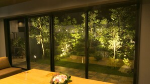 Una habitación con una mesa de madera y una ventana que da a un jardín de noche.