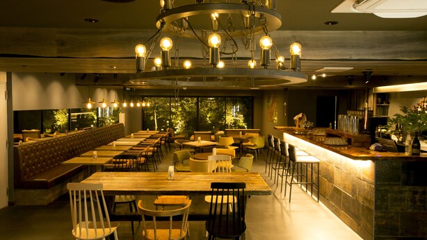 Un restaurante con una barra larga, varias mesas y una zona de bar.