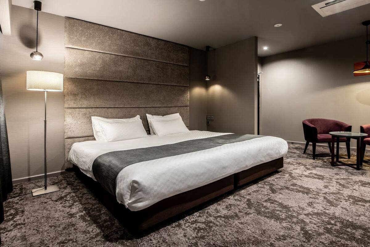 Una habitación de hotel moderna con una cama grande, una zona de estar con dos sillones y una lámpara de pie.