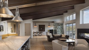 Een ruime woonkamer met een groot houten plafond, een keuken met een marmeren aanrechtblad en een zithoek met een bank en fauteuils.