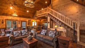 Interior acogedor de una cabaña de troncos con sala de estar, comedor, cocina y una escalera de madera.