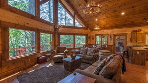 Una cabaña espaciosa con amplias ventanas, una zona de estar acogedora con sofá y sillones, una mesa de comedor de madera y una barra.