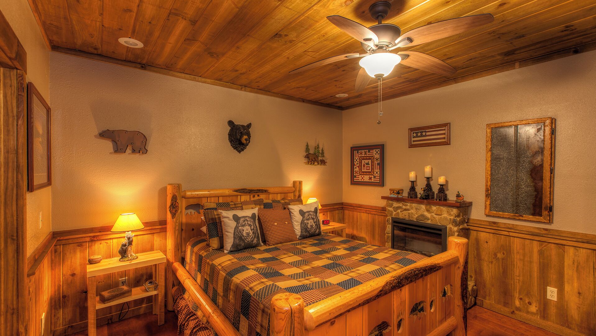 A cozy bedroom with a wooden ceiling, a bed with a patterned quilt, a fireplace, and wall decorations including animal heads and a flag.