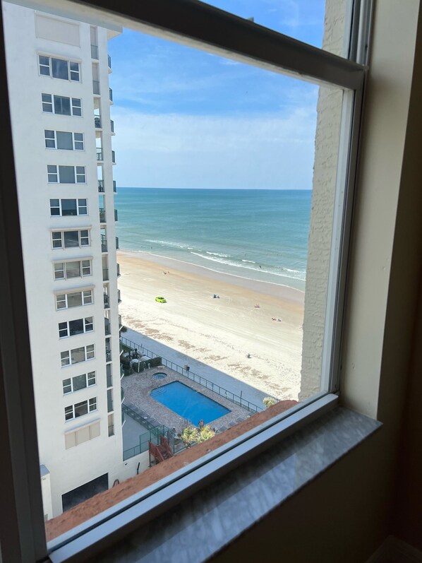 Vista da janela com uma praia, piscina e um edifício alto.