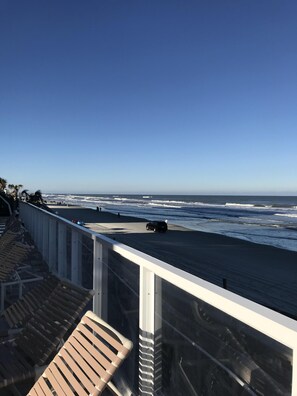 Un balcon avec vue sur l’océan, une plage de sable et quelques personnes qui se promènent.