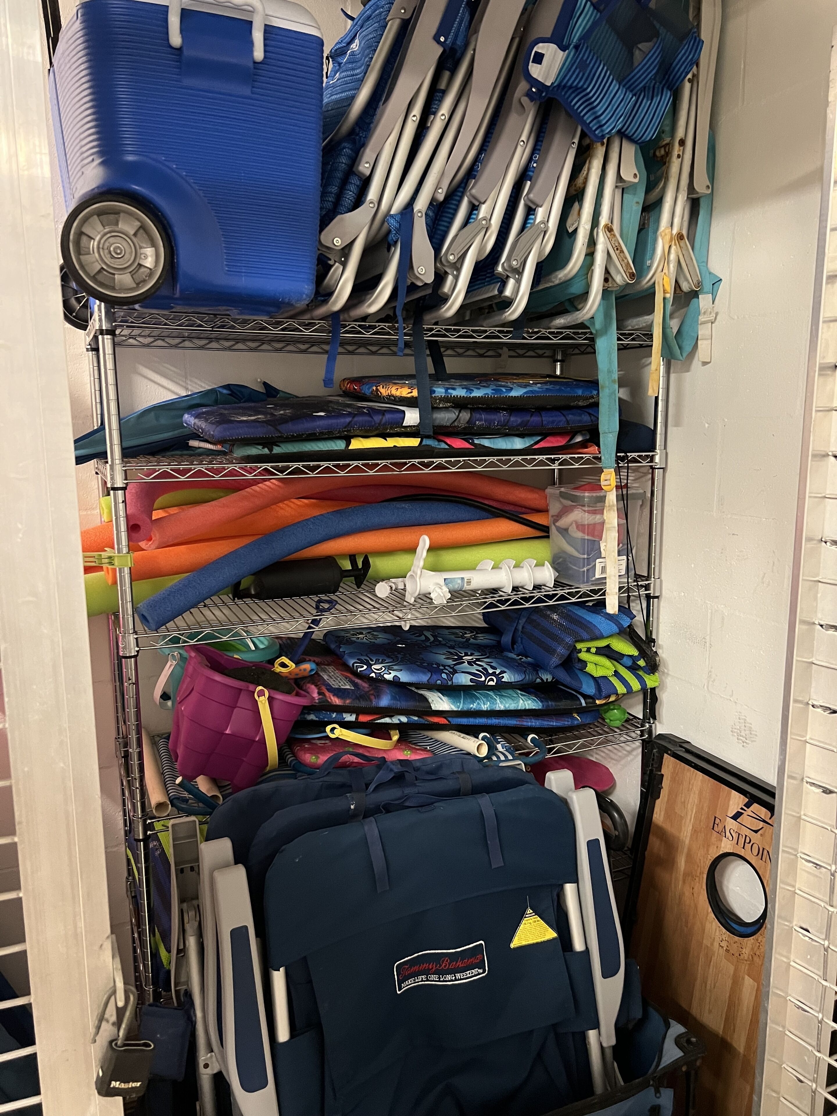 Un área de almacenamiento con estantes que contienen diversos objetos, como esteras enrolladas, bolsas y una maleta azul.