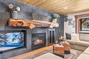 A modern living room with a fireplace, a mounted TV, and a wooden log shelf.