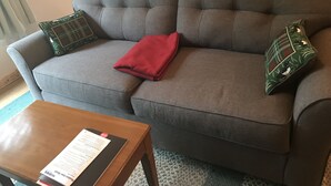 En grå soffa med en röd pläd, två mönstrade kuddar och ett träbord som används som soffbord, med en meny på.