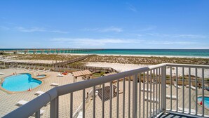 Vista de una playa con piscina, sillas de descanso y un muelle al fondo.
