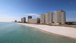 Un hotel frente a la playa con varios edificios altos, una playa de arena y aguas azules cristalinas.