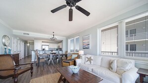 Un salón amplio con sofá blanco, mesa de centro de madera y una zona de comedor con sillas, y una cocina al fondo.