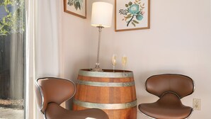 Una stanza con due poltrone in pelle marrone, un tavolino in legno con due bicchieri di champagne, una lampada e due quadri floreali incorniciati appesi al muro.