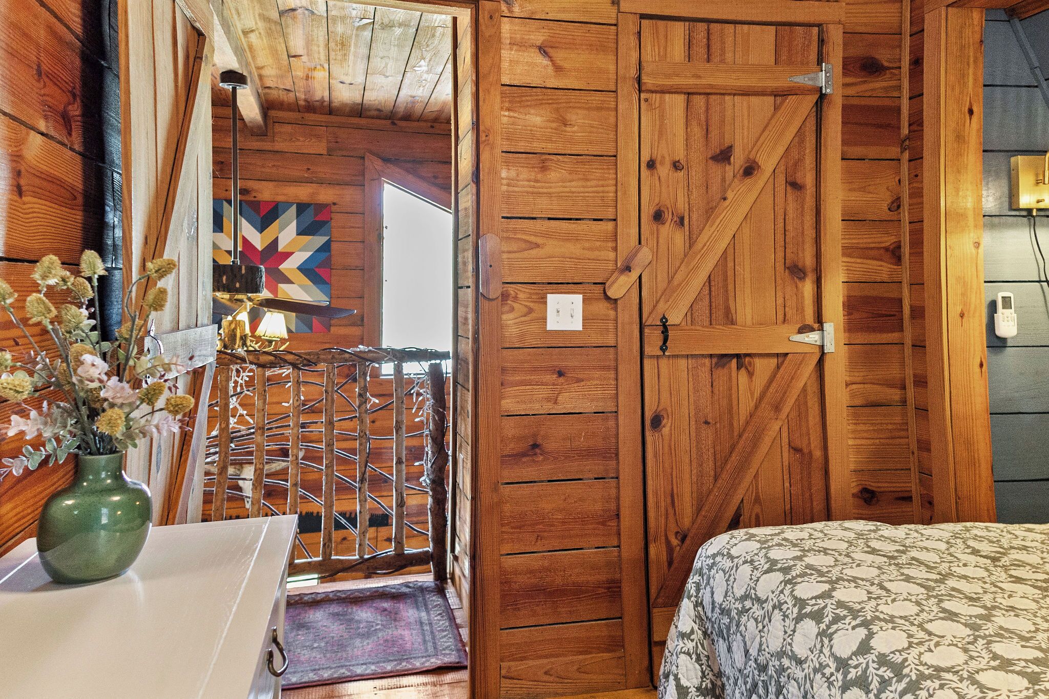 A wooden room with a bed, a door, and a view of a colorful wall.