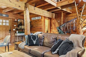 L’intérieur d’une cabane en bois, avec un canapé en cuir, une enseigne indiquant « ÉPICERIE » et un escalier.
