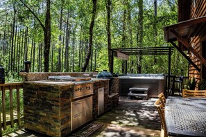 An outdoor kitchen area with a stone countertop, a grill, and a hot tub. - Hideaway Haven – A Private Retreat on 100 Acres (Marion)