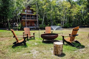 A rustic cabin with a deck, surrounded by a grassy area with Adirondack chairs and a fire pit. - Hideaway Haven – A Private Retreat on 100 Acres (Marion)